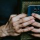 A person holds a smartphone and a book with an ornate cover, clasped together in both hands.