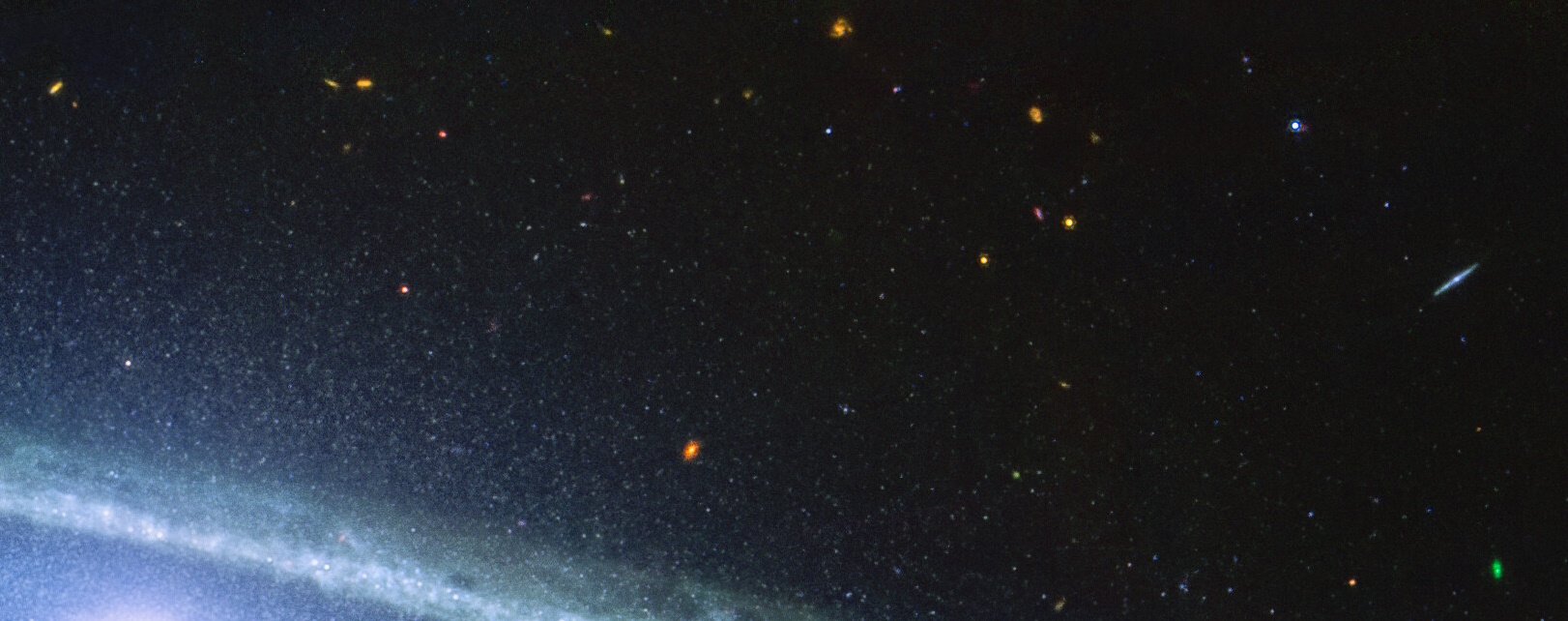 A view of space with numerous distant stars and galaxies against a dark background. The edge of a spiral galaxy, likely captured by the JWST, is visible at the bottom left corner, reminiscent of the iconic Sombrero Galaxy.