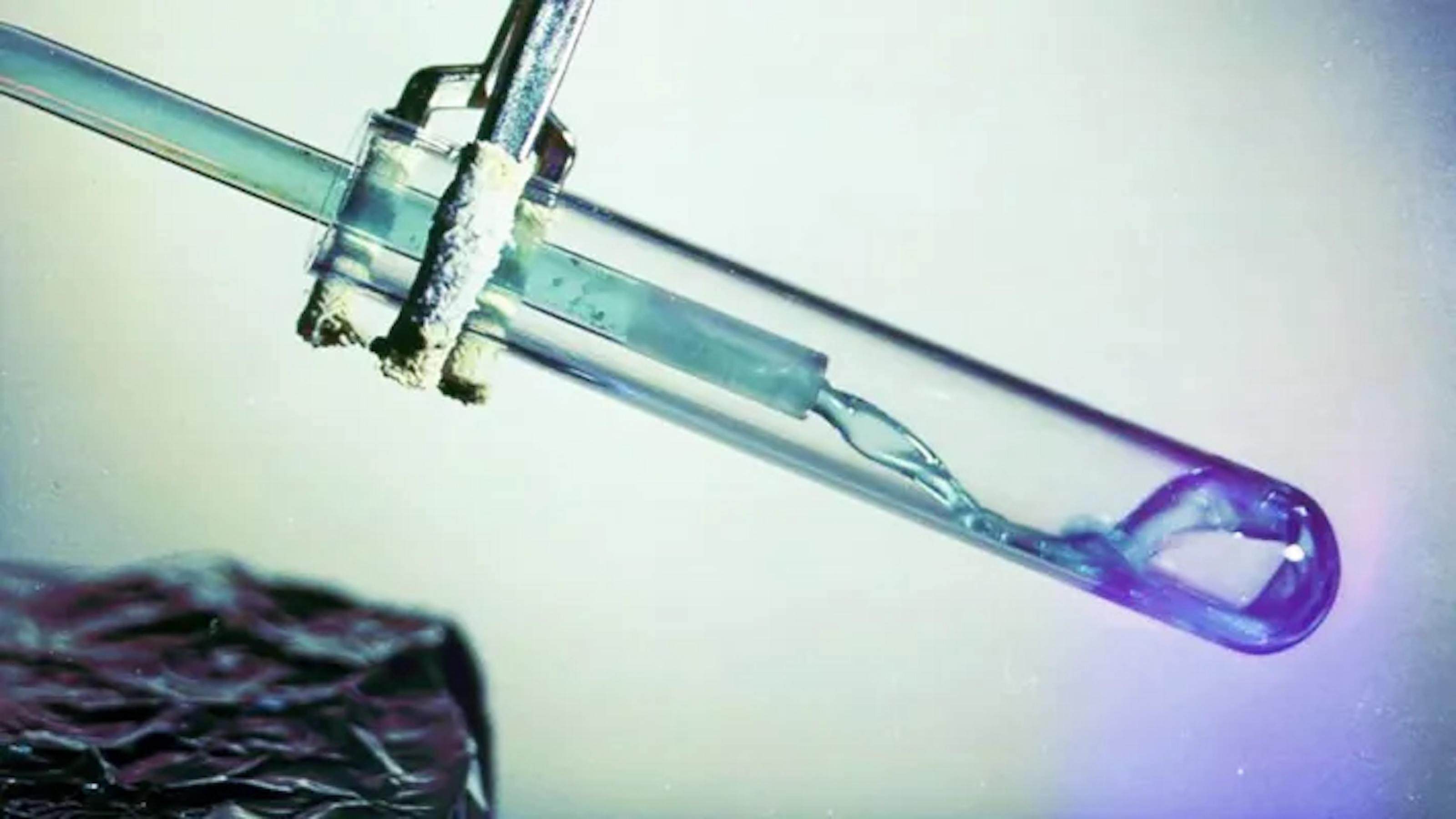 A test tube with a clamp holds a clear liquid and a glass rod inside, evoking the precision of nuclear research, set against a neutral background.