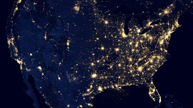 Satellite view of the United States at night reveals illuminated cities and areas, with dense clusters of lights in the eastern region, highlighting vibrant economic hubs reminiscent of workforce data concentrations, contrasted by the sparser illumination in the western regions.