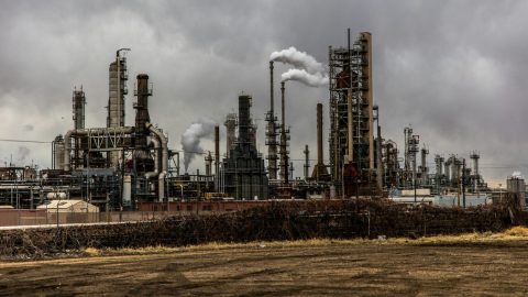 Industrial landscape featuring large smokestacks and various structures of an oil refinery, some incorporating cutting-edge carbon removal technology, set under a cloudy sky.