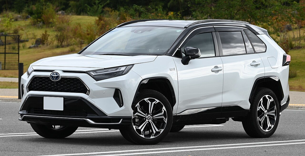 White SUV parked on a road, featuring a modern design with black accents and alloy wheels. Trees and grass are visible in the background.