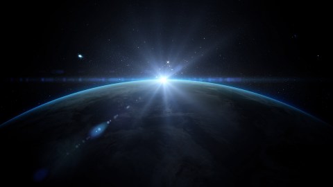 View of the Earth from space with the sun peeking over the horizon, surrounded by stars in a dark sky.