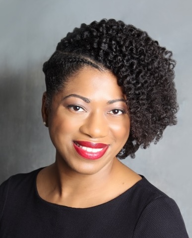 Person with curly hair and red lipstick smiling, wearing a black top against a gray background.