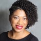 Person with curly hair and red lipstick smiling, wearing a black top against a gray background.