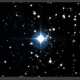 A bright star emits light in a field of smaller, scattered stars against a dark sky.