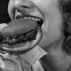 Black and white close-up of a woman savoring a burger wrapped in paper, her eyes reflecting her elevated taste expectations.