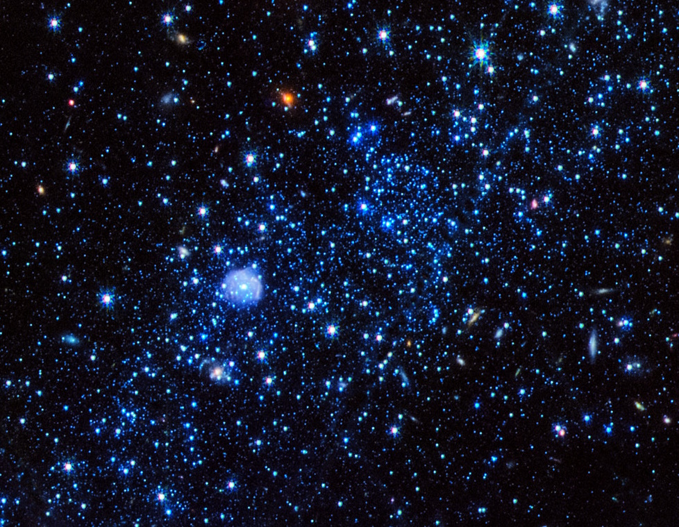 A dense cluster of blue stars and isolated galaxies in space, interspersed with glowing celestial bodies against a dark background, seems to grow ever more intricate.