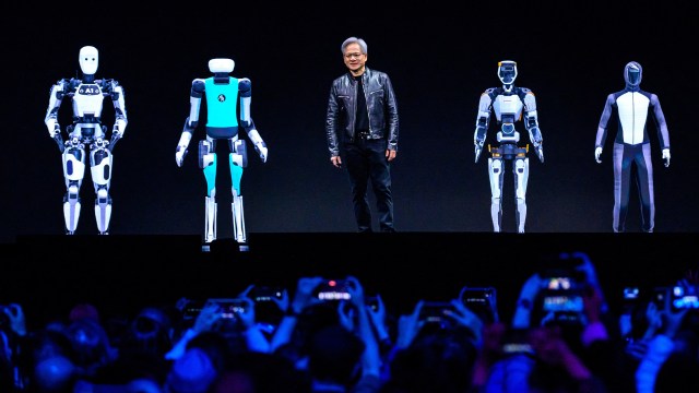 A person stands on stage with four humanoid robots, powered by NVIDIA technology, presenting to an eager audience.