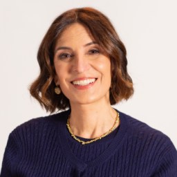 Suzy Welch wearing a navy sweater and gold jewelry against a plain background.