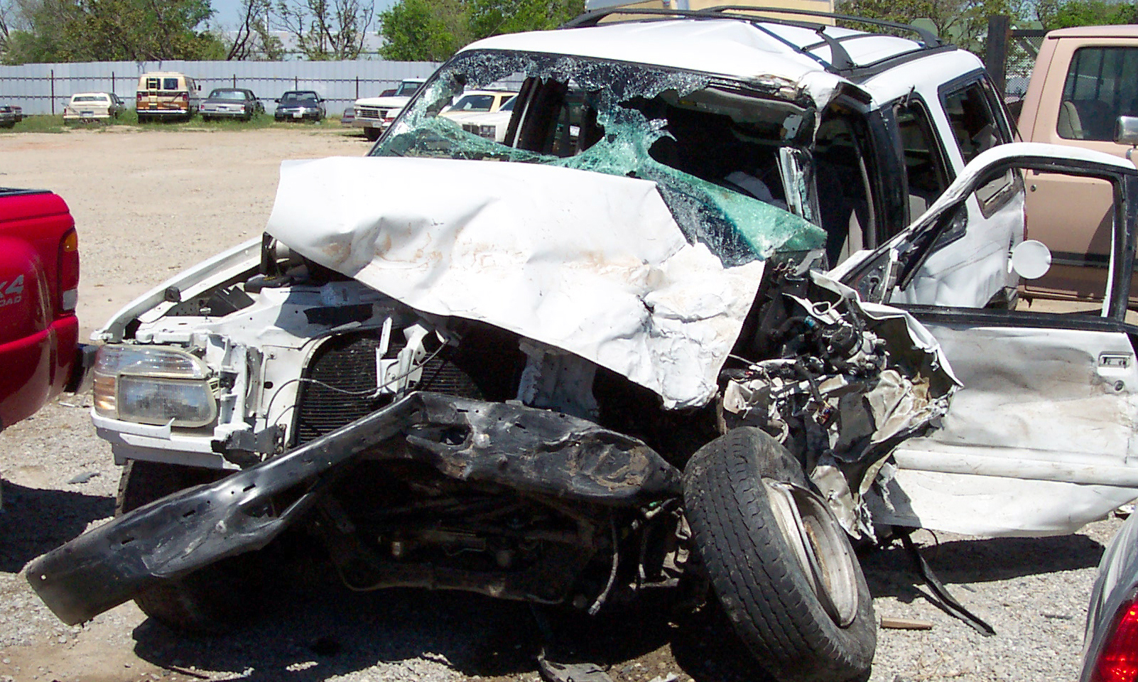 A severely damaged white SUV, with a crushed front end and shattered windshield, stands as an unsettling testament to the ignorance of safety protocols. It rests silently amidst other vehicles in the lot, each telling its own story.