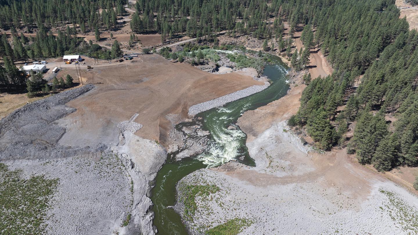 Aerial view of a river winding through a forested area with visible cleared land and structures nearby.