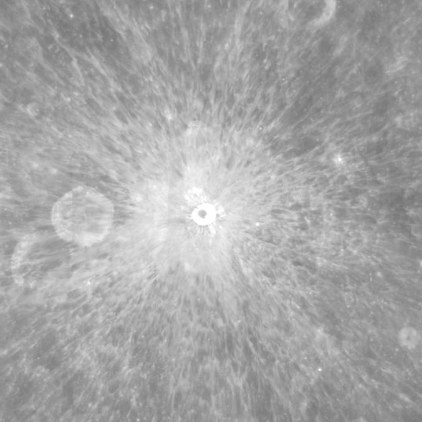 A grayscale image of the moon's surface features a large crater at its center, reminiscent of a celestial Grand Canyon, surrounded by radial ejecta patterns. Numerous smaller craters are scattered throughout.