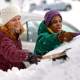 Two people experience everyday enlightenment as they shovel snow off a car in a winter wonderland, bundled up in cozy jackets, hats, and gloves.