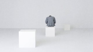 An introverted leader in a gray suit sits thoughtfully on a white cube in a minimalist, white space with two other white cubes nearby, embodying the power of quiet contemplation.