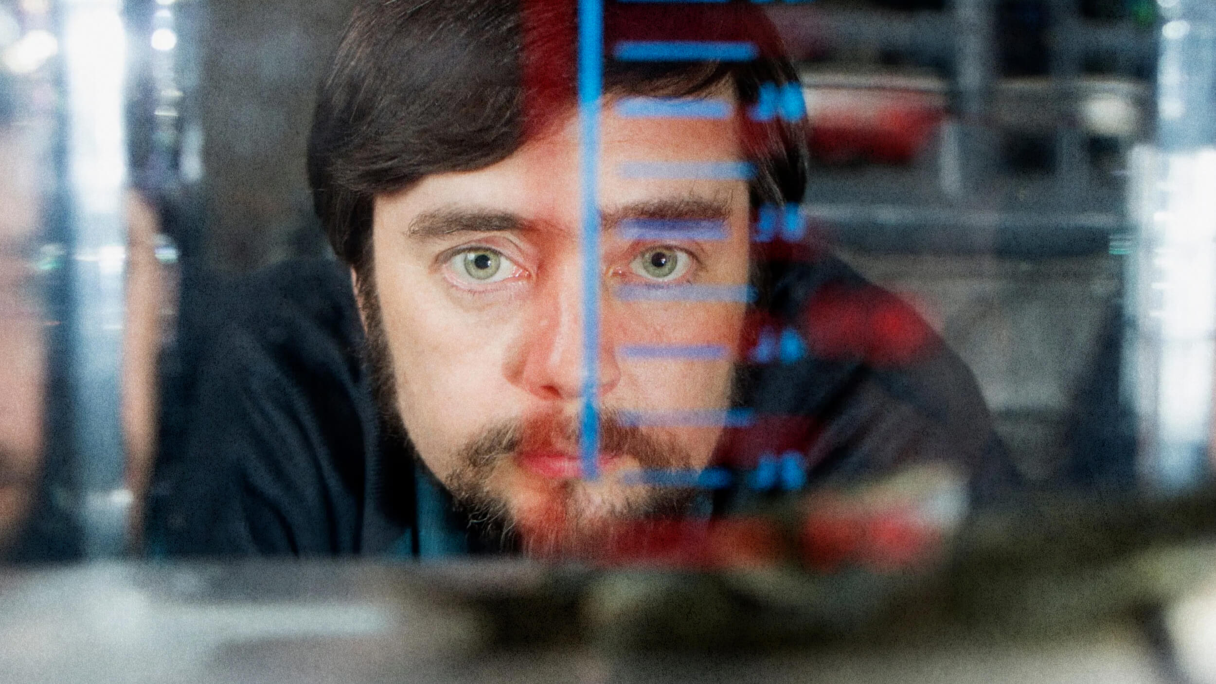 Man peering through a glass container with measurement markings, focused expression, blurred foreground.