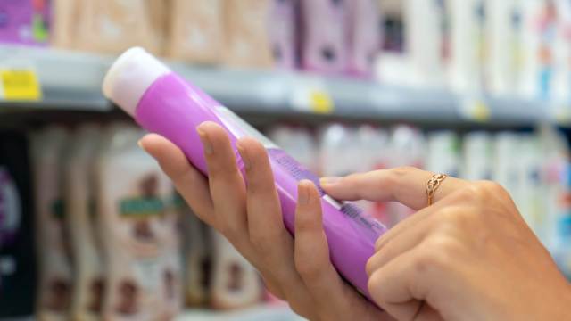 In the store aisle brimming with products, a person examines the label of a purple bottle, curious about the latest scienceploitation claims that promise groundbreaking benefits.