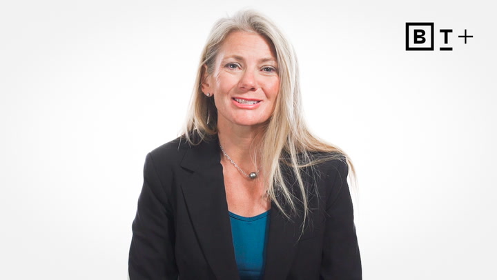 A woman with long blonde hair in a black blazer and blue top sits against a plain white background with a "BT+" logo in the top right corner.