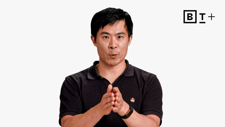 A man in a black polo shirt gestures with his hands while speaking. The background is plain white with a "B T +" logo in the top right corner.