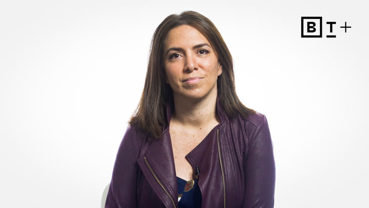 A woman with straight brown hair wearing a purple jacket sits against a white background with a "B T +" logo in the top right corner.