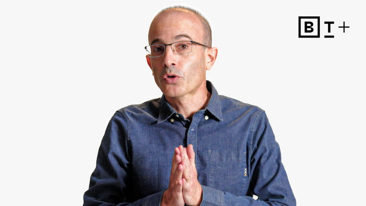 A man wearing glasses and a blue button-up shirt speaks with hands clasped, in front of a plain white background with a "B T +" logo in the corner.