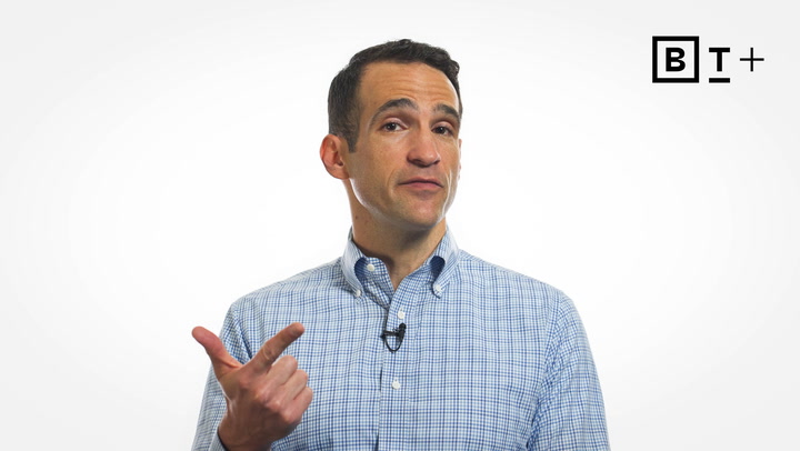 A man in a blue checkered shirt stands against a white background, gesturing with his left hand. A "B T +" logo appears in the top right corner.