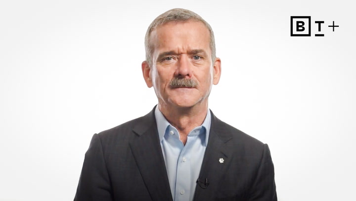 A man in a suit and collared shirt stands against a plain white background with a "BT+" logo in the top right corner.