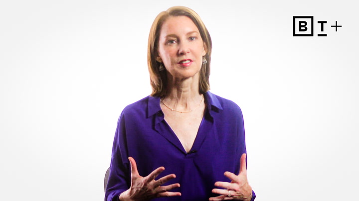 A woman with shoulder-length brown hair wearing a purple blouse speaks while gesturing with her hands; a "B T +" logo is in the top right corner.