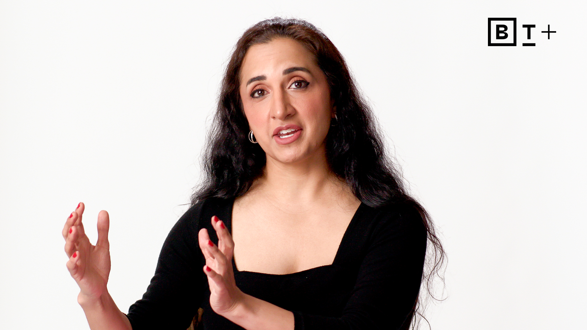 A woman with long dark hair gestures while speaking in front of a white background, with the BT+ logo displayed in the top right corner.
