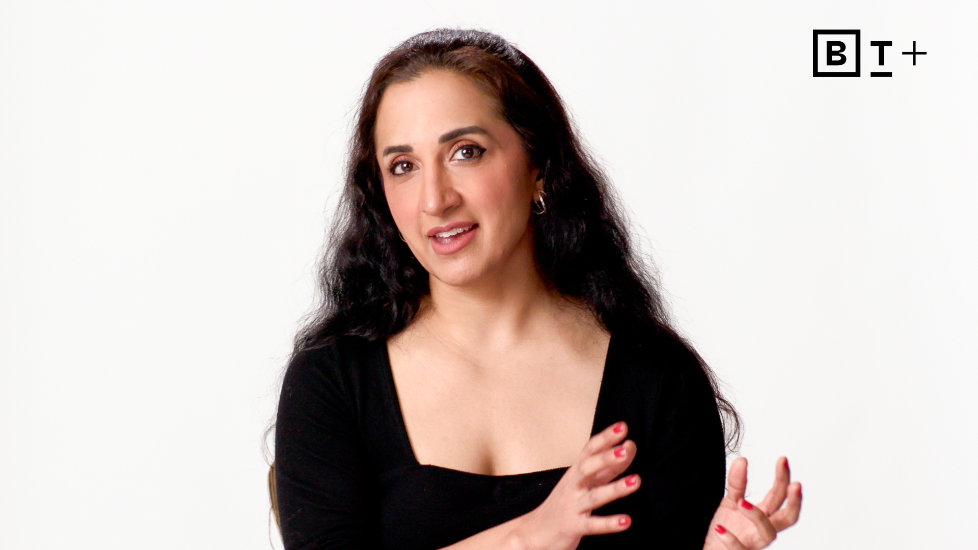 A woman with long dark hair and a black top gestures with her hands while speaking against a plain white background; BT+ logo is in the top right corner.