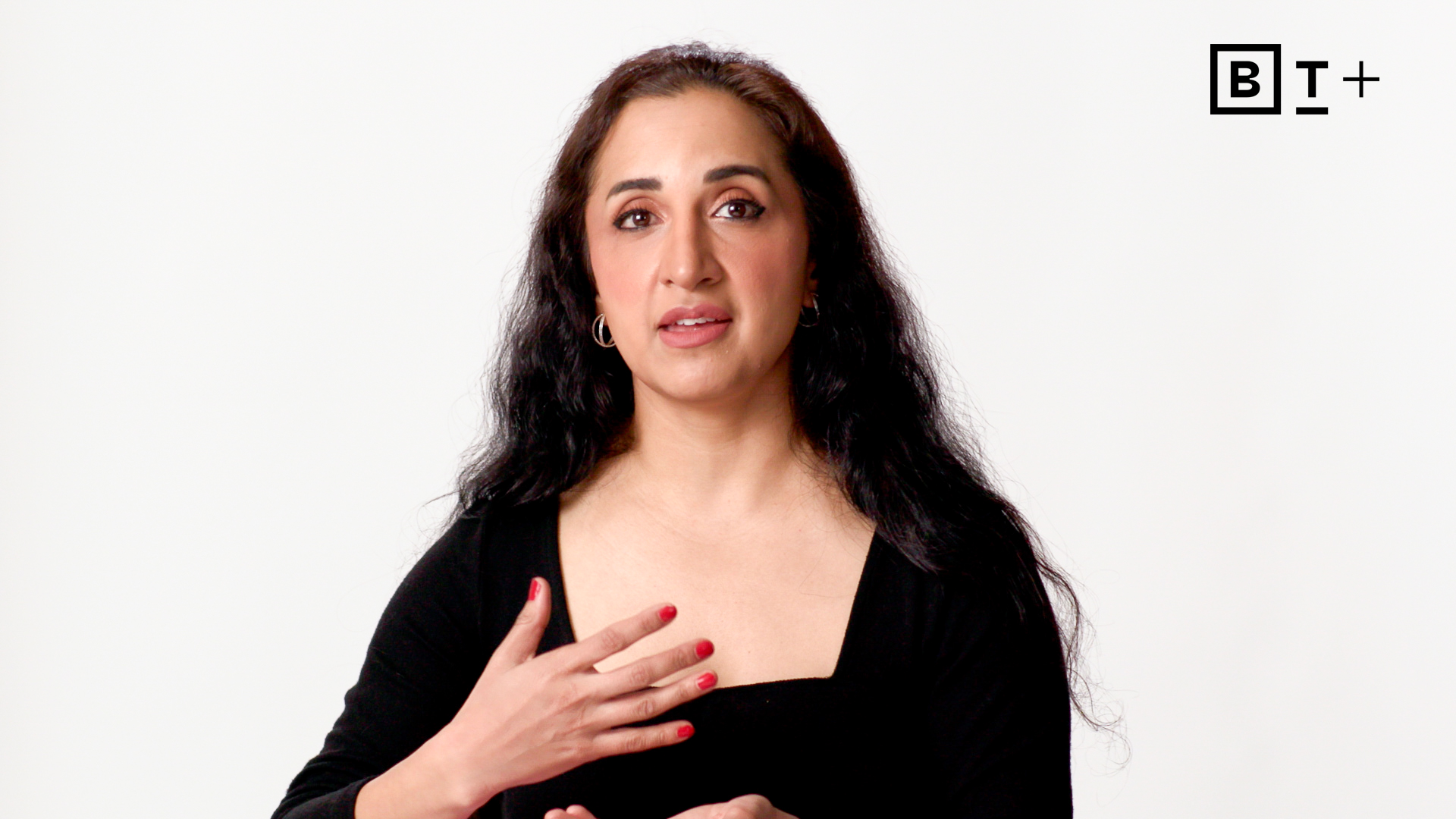 A woman with long dark hair and a black top gestures with her hand against a plain white background. The BT+ logo is visible in the top right corner.