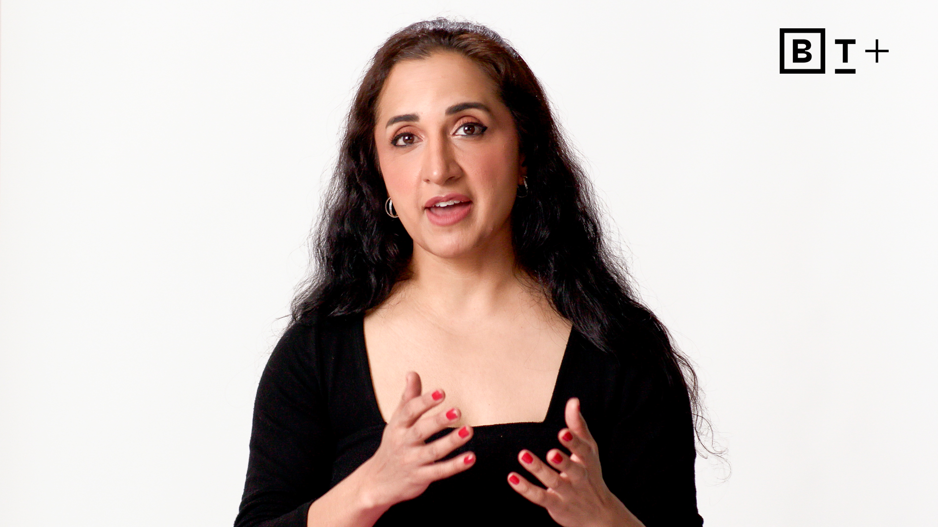 A woman with long dark hair and red nail polish gestures while speaking against a plain white background with the BT+ logo visible in the top right corner.