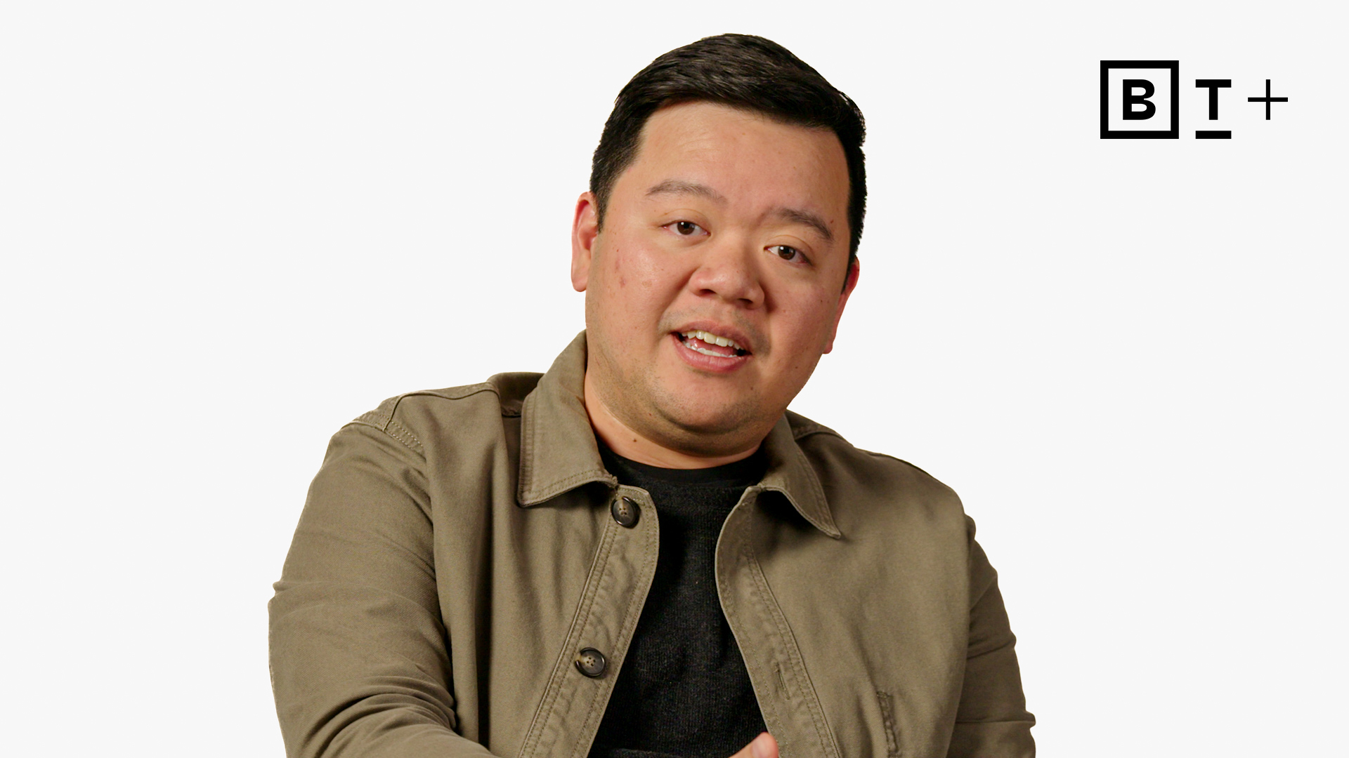 A person sits against a plain white background, wearing a khaki jacket over a dark shirt. The BT+ logo is visible in the top right corner.