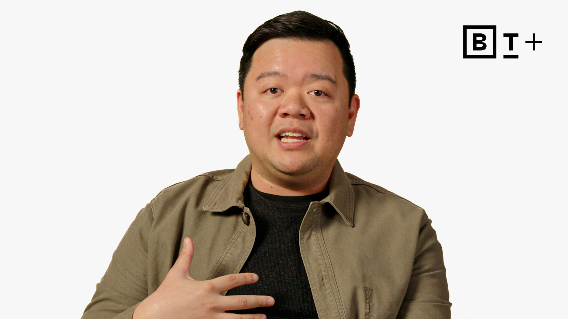 A person sits against a plain white background, speaking and gesturing with one hand on their chest. The letters "BT+" appear in the top right corner.