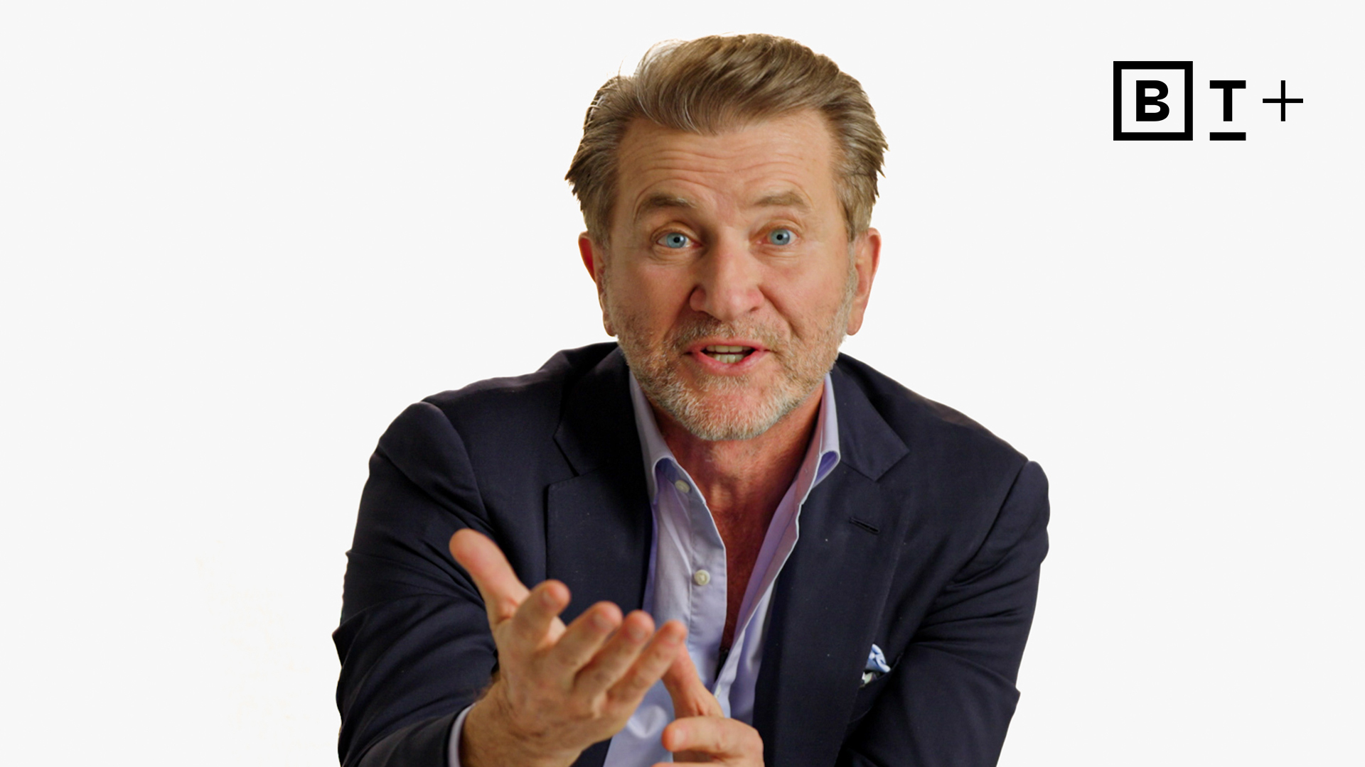 A man in a navy blazer gestures with his right hand while speaking. The background is white with a "B T +" logo in the top right corner.