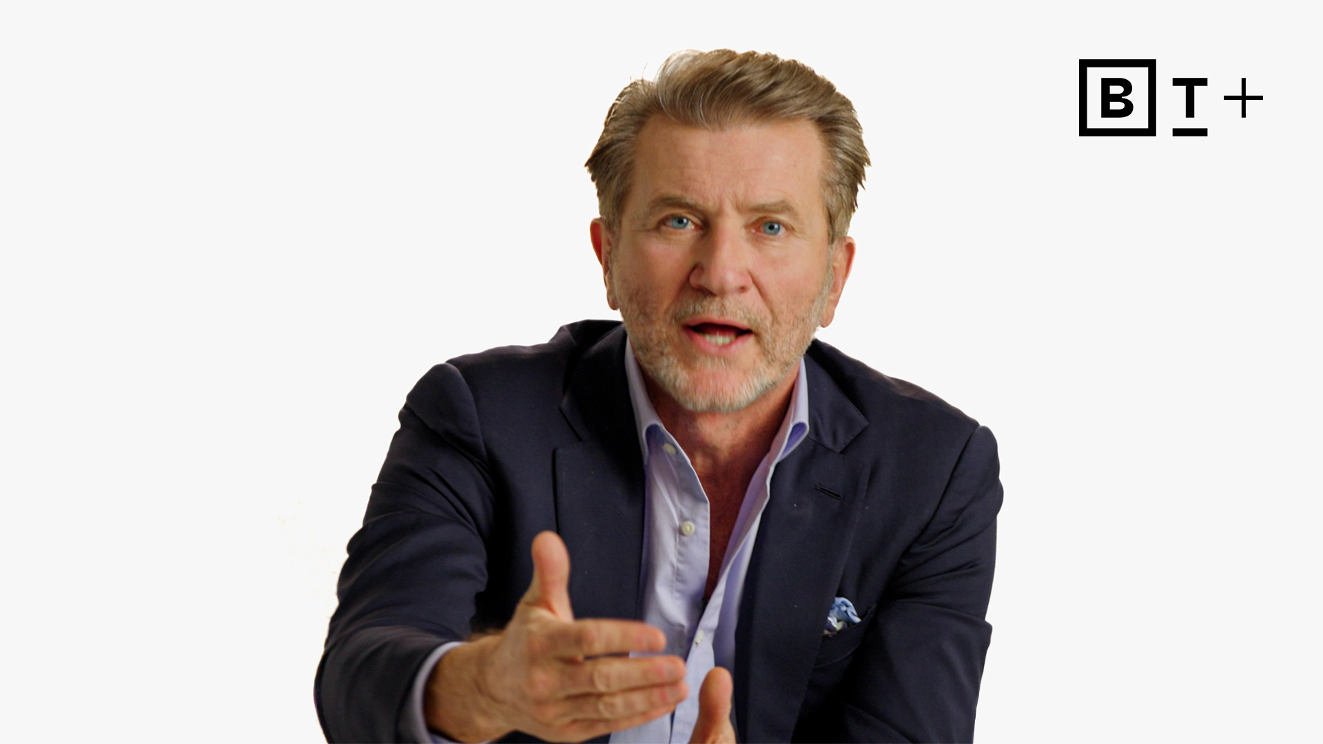 A man in a navy blazer gestures with his right hand while speaking. The background is plain white with a "BT+" logo in the top right corner.
