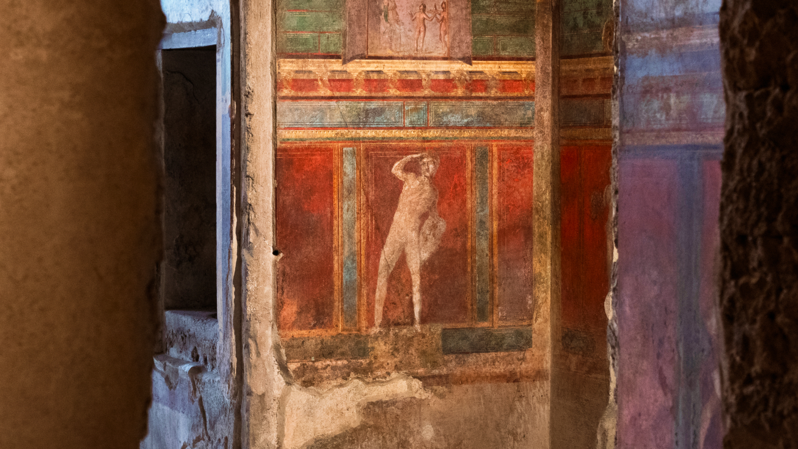 Ancient wall fresco depicting a standing human figure, surrounded by red, green, and brown decorative panels—an evocative remnant bearing the marks of history’s lost voices and the passage of time.