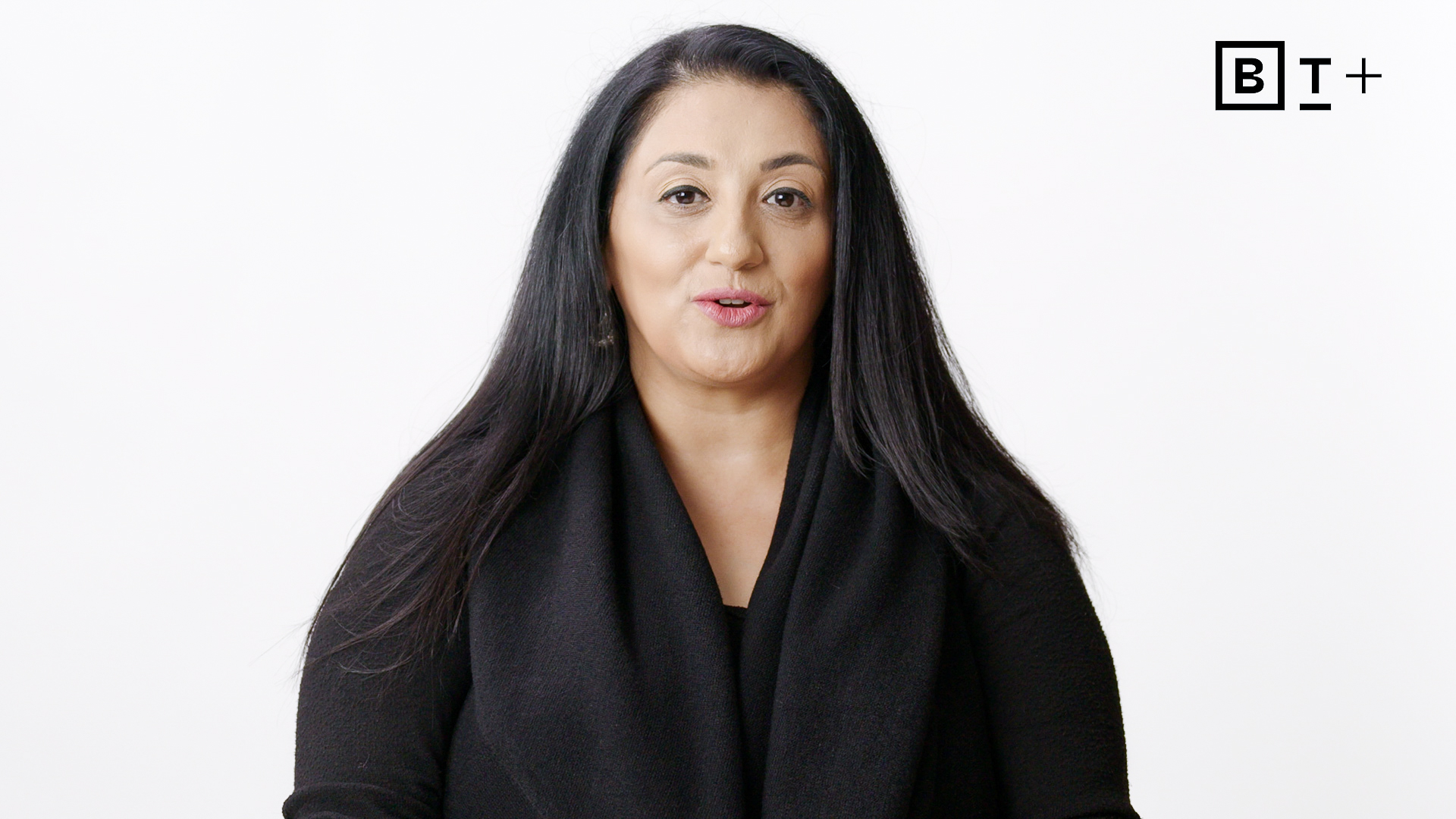 A woman with long black hair wearing a black top sits against a plain white background with the "B T +" logo in the top right corner.