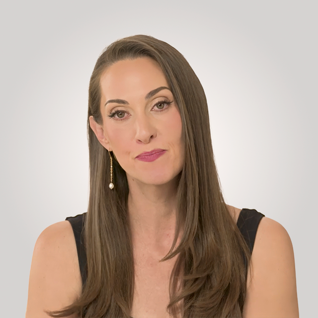A woman with long brown hair wearing a black sleeveless top and a single dangling earring poses against a plain light background.